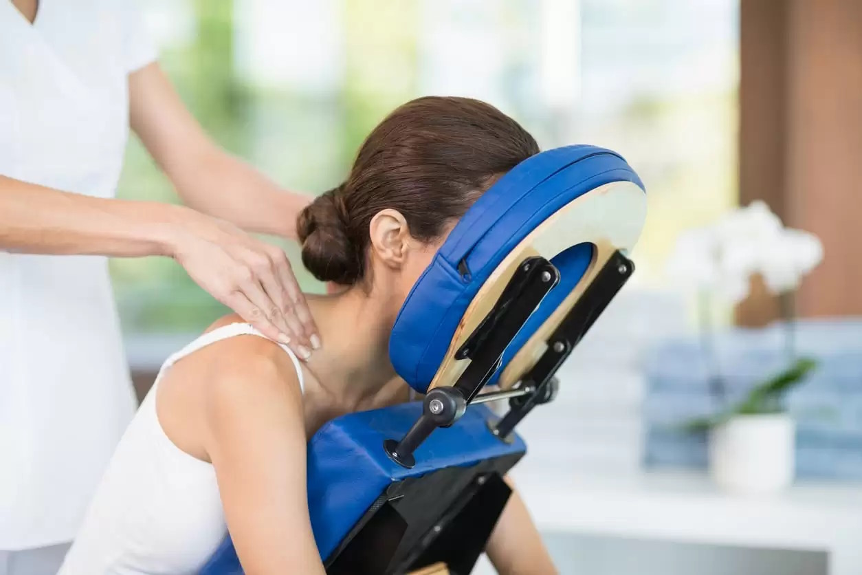 Een klant die met haar gezicht tegen een stoel leunt en een massage krijgt